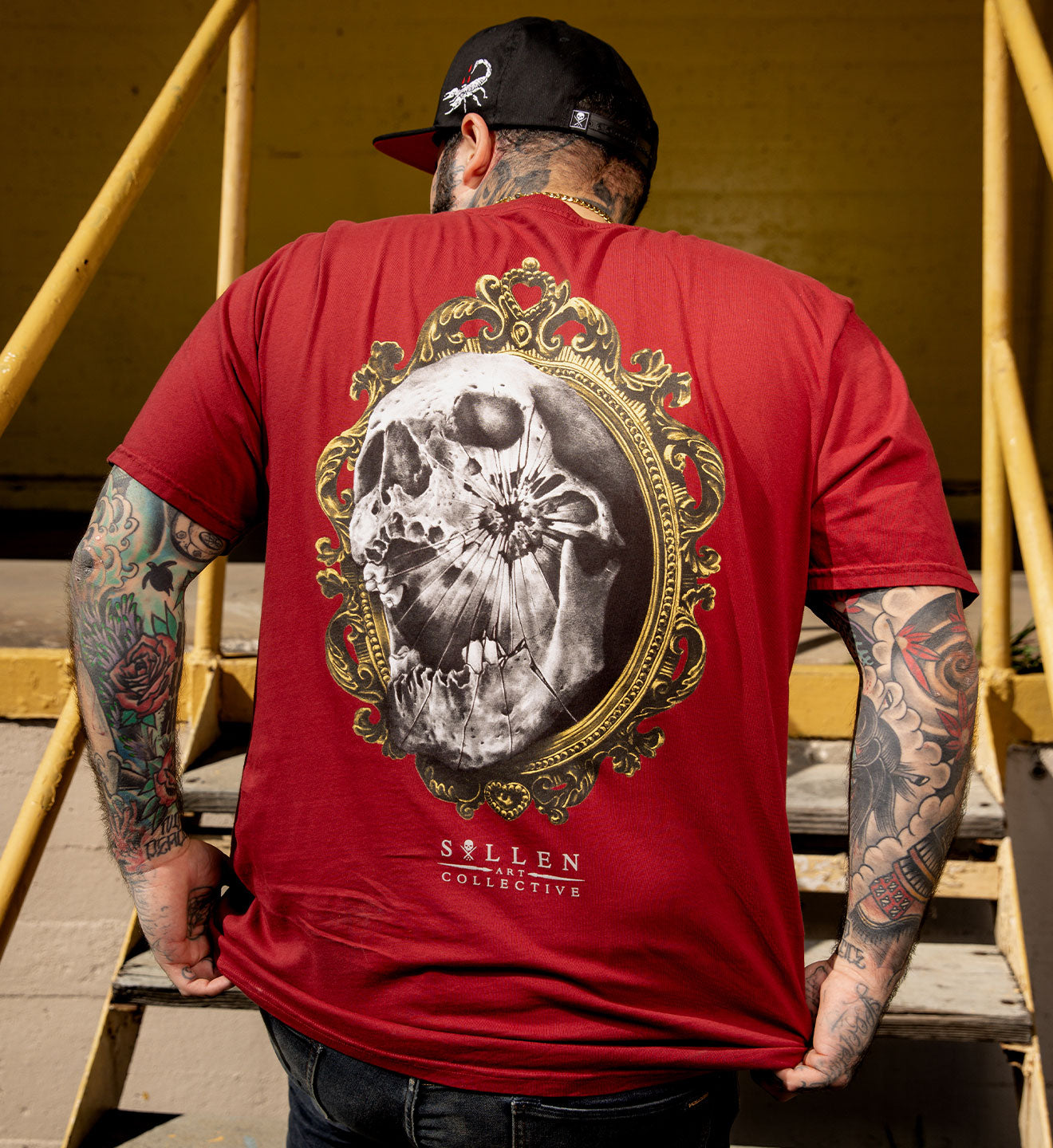 Man wearing a red t-shirt with a skull design on the back, standing outdoors.