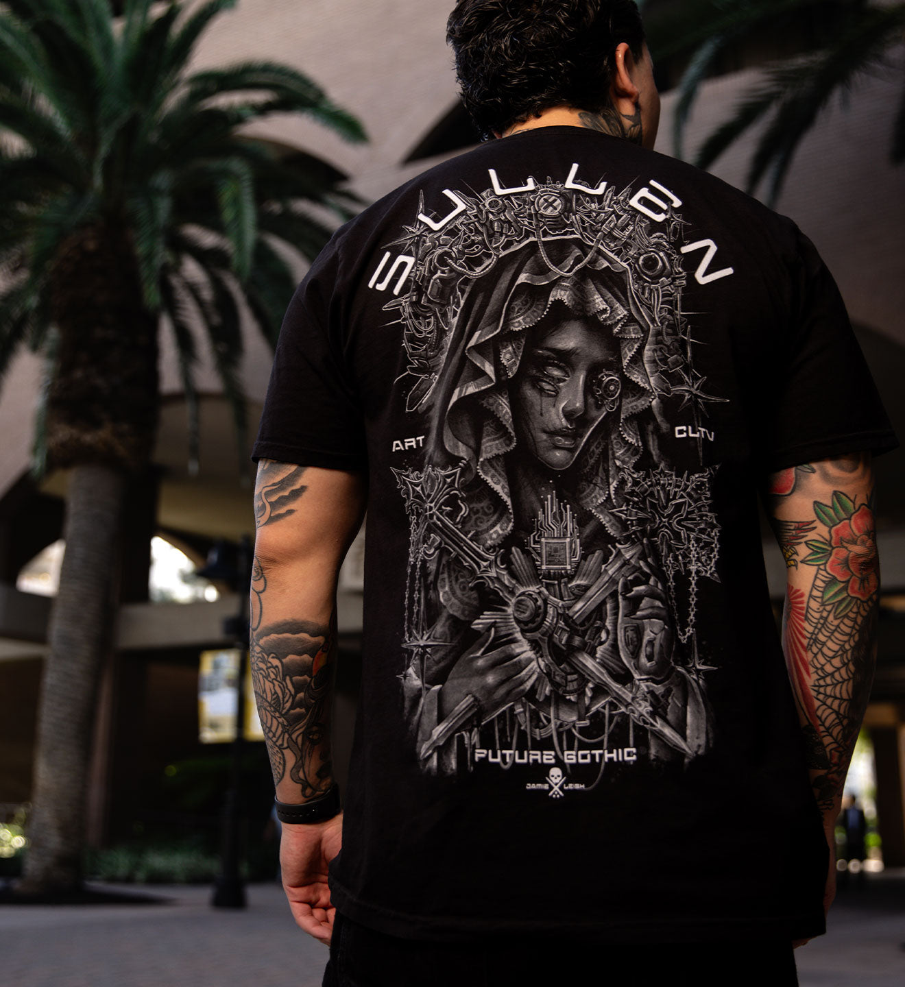 Person wearing a black t-shirt with intricate design and text, standing outdoors.